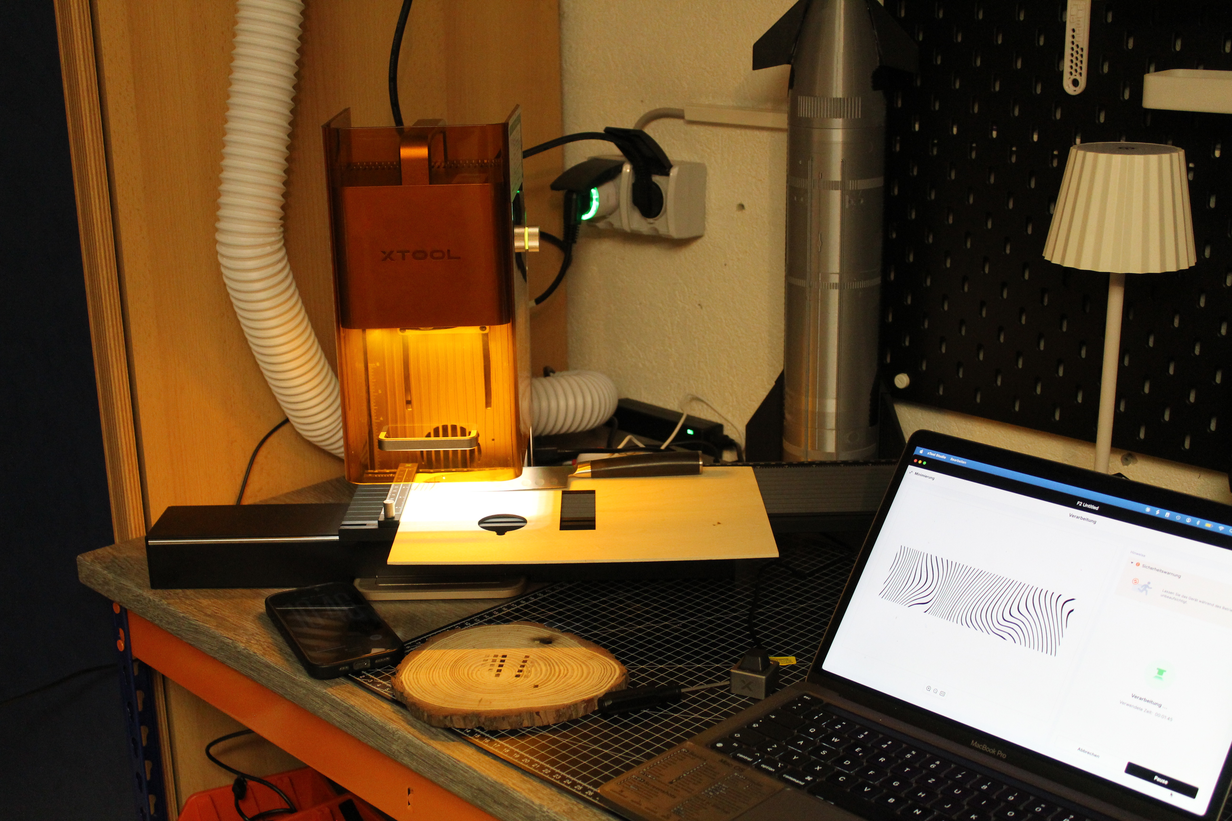 Lasergravur auf Holzscheibe neben Laser und Laptop